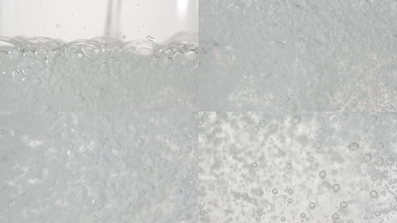 缓慢运动的水流落在光滑清洁的表面上，产生气泡，下落后水滴飞溅。在轻背景下倒入透明容器中的透明液体的新