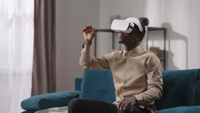 虚拟现实娱乐小工具，头戴式显示屏的黑人独自坐在房间里，用手滑动虚拟屏幕