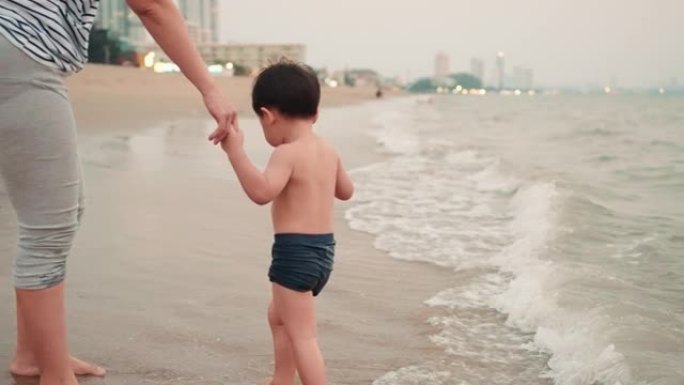 母亲牵着小儿子在芭堤雅海滩上一起玩。