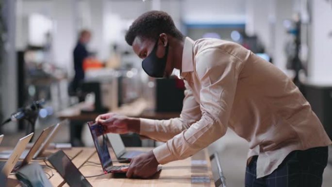 年轻的非洲裔美国人正在电子商店测试现代笔记本电脑，观看展览样本