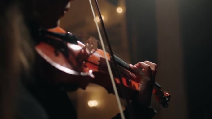 穿着黑色衣服的女小提琴手在黑暗的爱乐音乐厅演奏经典音乐
