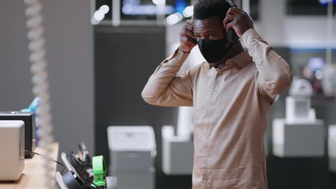 带面罩的非洲裔美国人正在音频设备商店选择现代耳机，在家用电器商店购物