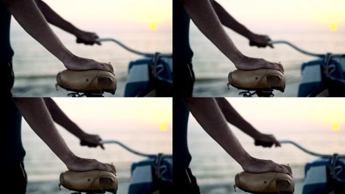 日落时海滩上自行车座椅上男人的手的细节照片