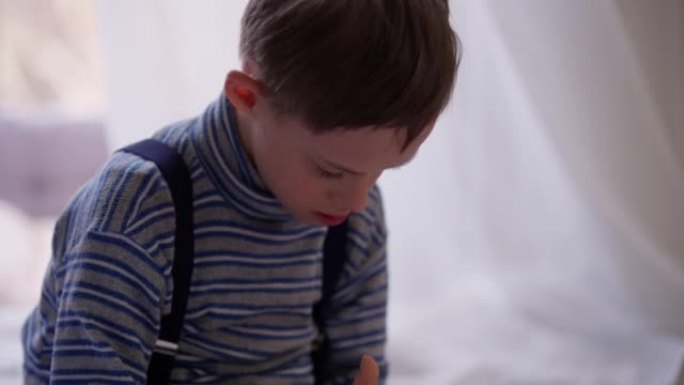 集中古玩自闭症男孩坐在舒适的室内智能手机上玩耍的肖像。专注的高加索儿童在手机游戏中享受游戏的基座镜头