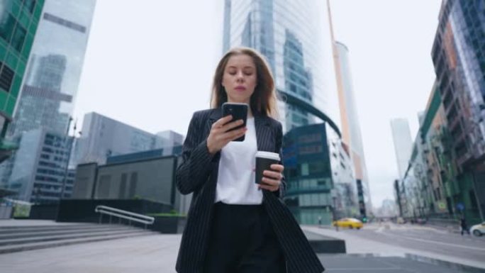 成功的女商人早上走在城市里，用着智能手机，喝着咖啡