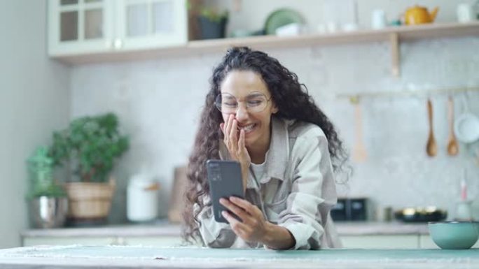 戴着眼镜的惊讶女人在家里看了手机留言后非常开心兴奋卷曲黑发看着智能手机屏幕