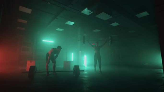 训练专业的举重运动员，男人和女人在黑暗的健身房举起杠铃，运动的人
