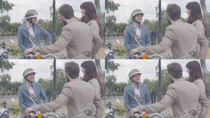 戴着自行车头盔的快乐成年男子坐在摩托车上，白人夫妇坐在踏板车上与他交谈。阴雨天与朋友休息的积极男性骑