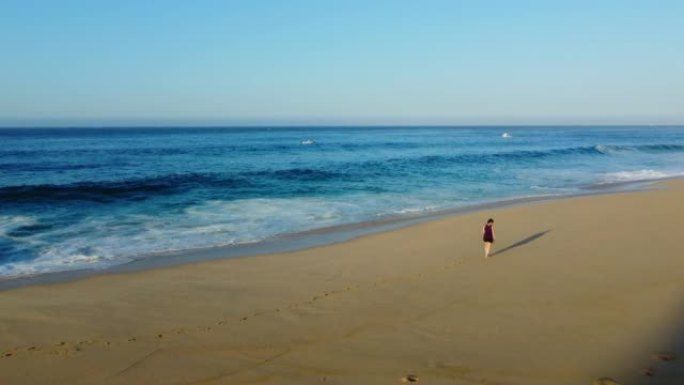 晴天，一名妇女在海滩上行走的空中无人机拍摄