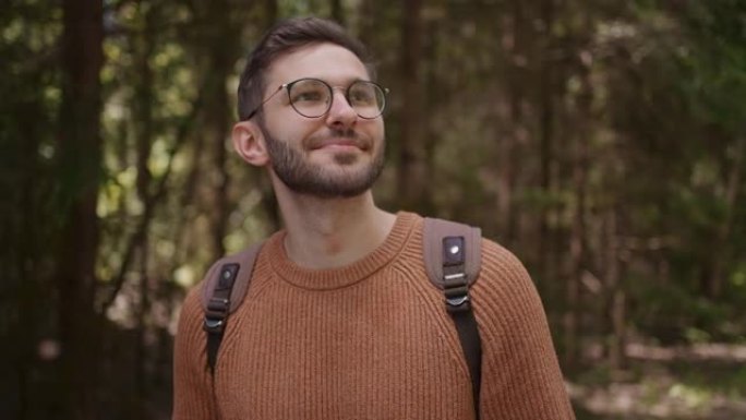 一个拿着手机和背包的男性旅行者穿过森林，公园。一个人微笑着，用手机搜索信息。