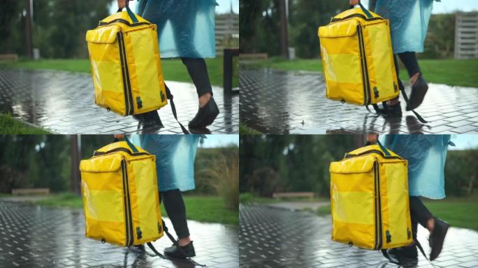 在城市公园散步时，身穿雨衣的无法辨认的快递员手里拿着黄色送货袋的追踪照片。年轻的白人男子背着背包在户