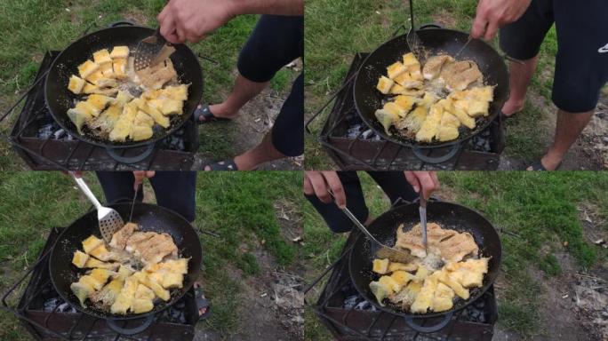 在着火的锅里烤长矛。小脆皮鱼片在油中油炸。自然界烹饪食物的概念。一个人准备食物，然后用抹刀翻转。浅景