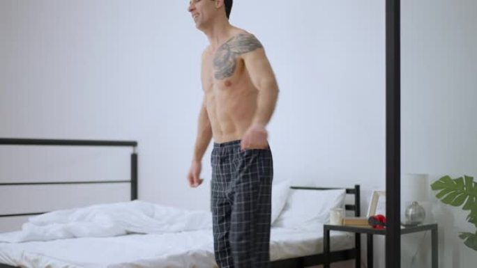 积极的中东男子走到床上摔倒。放松快乐的英俊纹身男人晚上在家休息在卧室。放松和睡眠概念。
