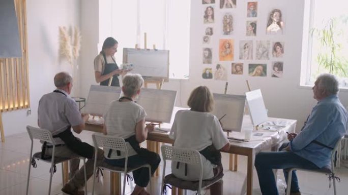 欢快的资深朋友在画布上绘画的高角度视图。高级女子在与小组一起画画时微笑。一起上绘画课的高年级学生。高