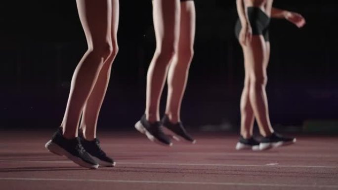 三名女运动员在路灯亮着的黑暗体育场准备田径比赛。一群女子在赛道上比赛前热身和集中注意力的延时镜头