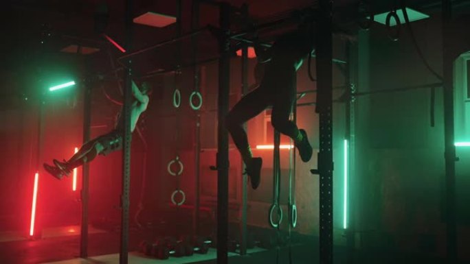 健身房里的两个男人和一个女人在黑暗的霓虹灯下一起在单杠上做引体向上。健身和训练的氛围