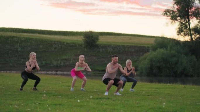 集体健身锻炼在大自然中，三名女运动员和英俊的健身教练在跳跃和蹲着