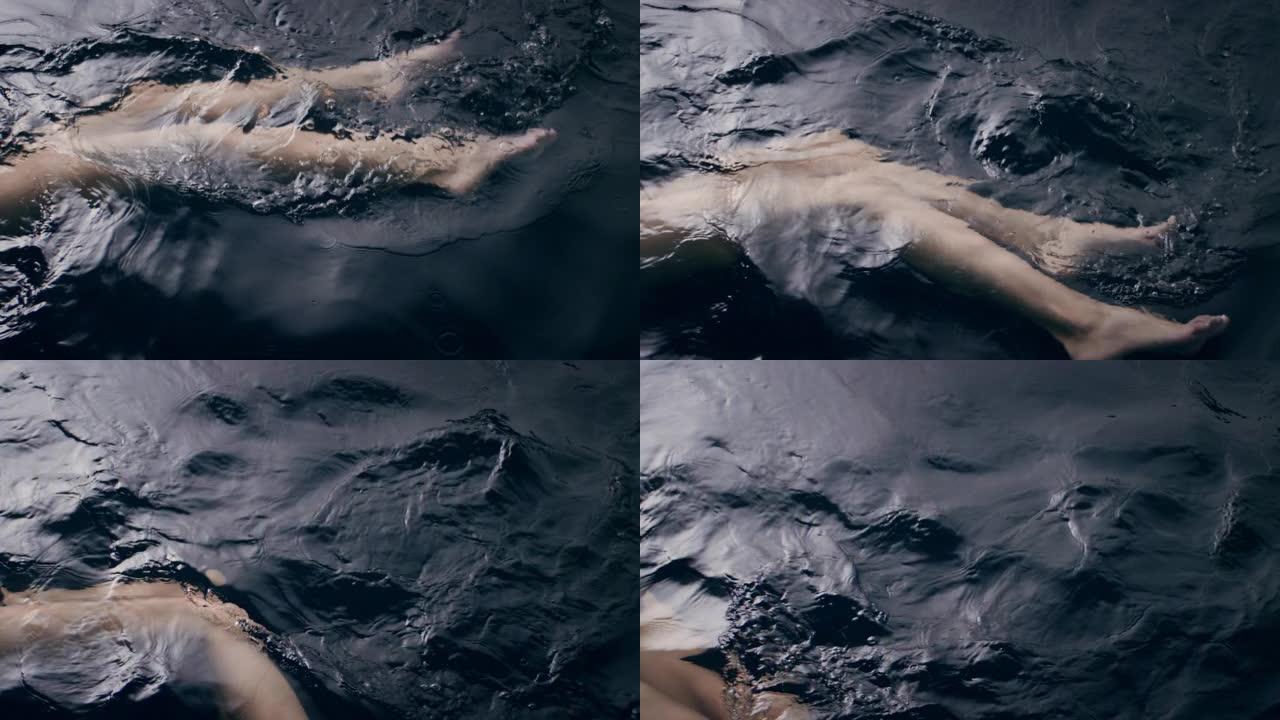 精致自然的女人漂浮在黑暗的水面上。腿部特写