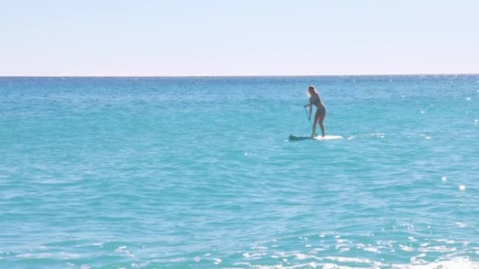 年轻的女飞行员在清澈的海水中站起来划桨板 (SUP)
