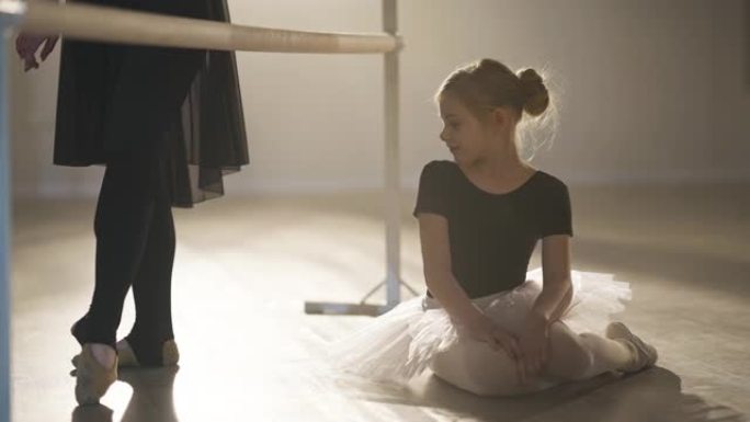 迷人的高加索女孩欣赏专业芭蕾舞演员的腿，在聚光灯下的舞步中移动，梦想着未来。舞厅工作室激励孩子的肖像