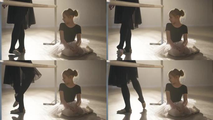 迷人的高加索女孩欣赏专业芭蕾舞演员的腿，在聚光灯下的舞步中移动，梦想着未来。舞厅工作室激励孩子的肖像