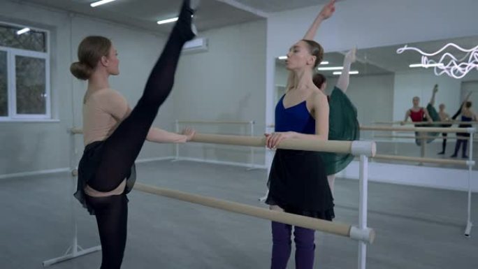 自信的职业芭蕾舞演员说话帮助朋友排练举起腿抱着巴雷。积极自信的白人女性在工作室室内跳交际舞。优雅和艺