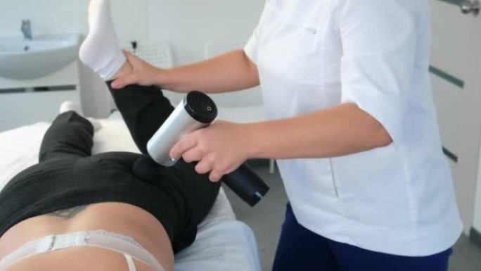 医生按摩师正在用电动按摩器按摩女性的臀部和腿部。
