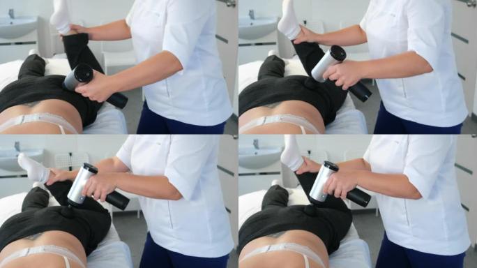 医生按摩师正在用电动按摩器按摩女性的臀部和腿部。