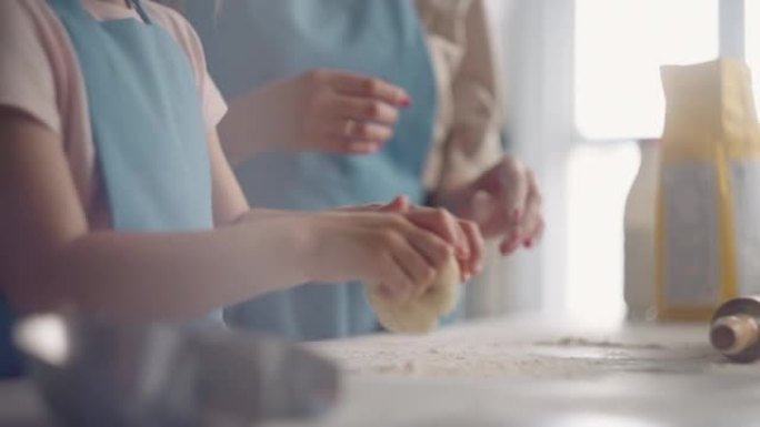 母亲在教小女儿在家做面包，孩子在桌子上揉面团