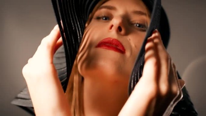 美丽诱人的金发女人用相机调情。穿着大而优雅的帽子摆姿势，用红唇遮住她的脸