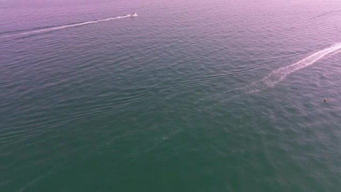 高角度镜头和海洋的鸟瞰图有了高速船，人们在英国伯恩茅斯海滩海滨享受着乐趣和最热的天气。
