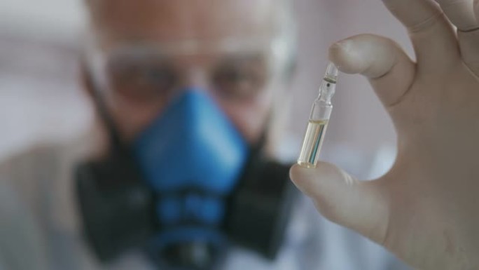 科学家在蓝色呼吸器和防护眼镜中的极端特写镜头，冠状病毒疫苗的开发者拿着白色透明安瓿。医生看了新疫苗。