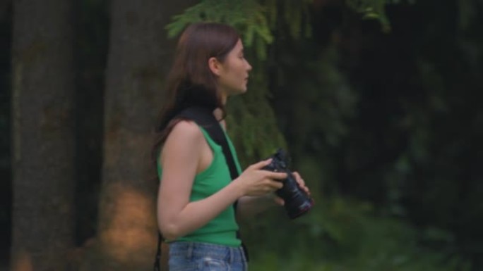 女孩摄影师拿着相机走在林地里寻找自然风景，拍照。旅行，爱好