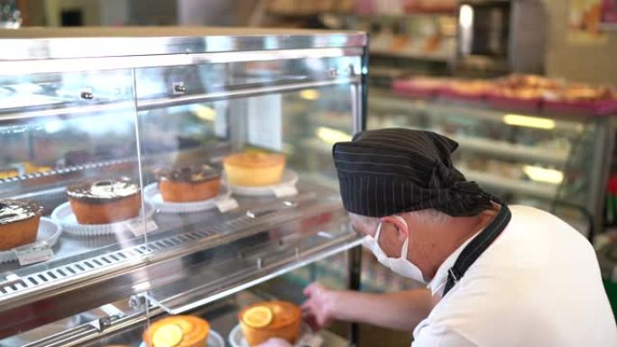 面包店员工在带有口罩的零售展示中安排蛋糕