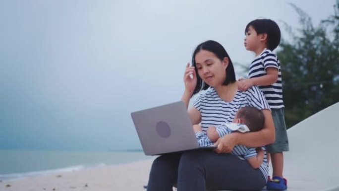 母亲和她的两个儿子在泰国的海滩上旅行时使用笔记本电脑。
