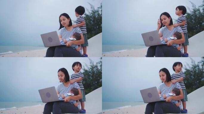 母亲和她的两个儿子在泰国的海滩上旅行时使用笔记本电脑。