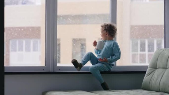 无忧无虑的童年时光，快乐的时刻，小男孩正在喝牛奶，在下雪的冬天早晨坐在窗台上