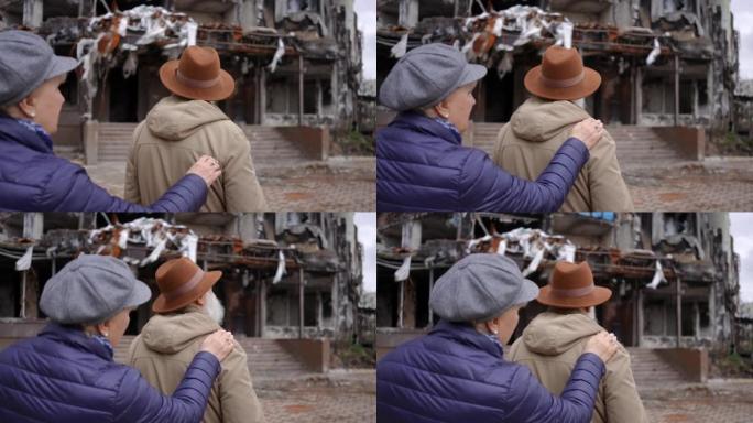 背影沮丧的老人看着被炸毁烧毁的居民楼，女人把手放在肩膀上支持配偶。老夫妇在城市外面的废墟房子里。缓慢