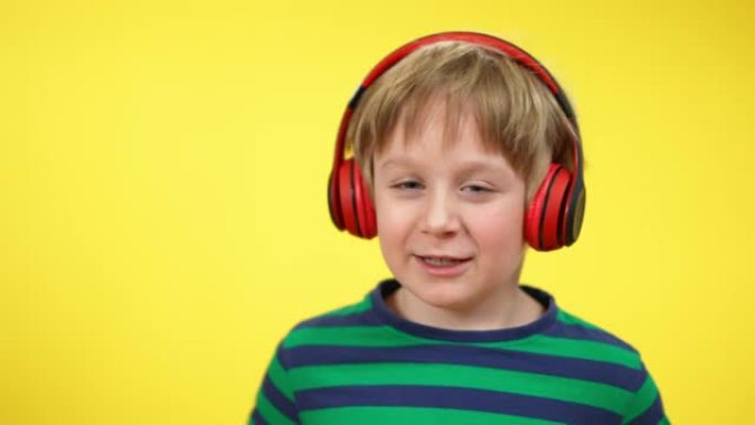 欢快迷人的高加索男孩在黄色背景下戴着耳机唱歌跳舞的特写镜头。积极快乐的孩子享受耳机播放列表音乐。爱好