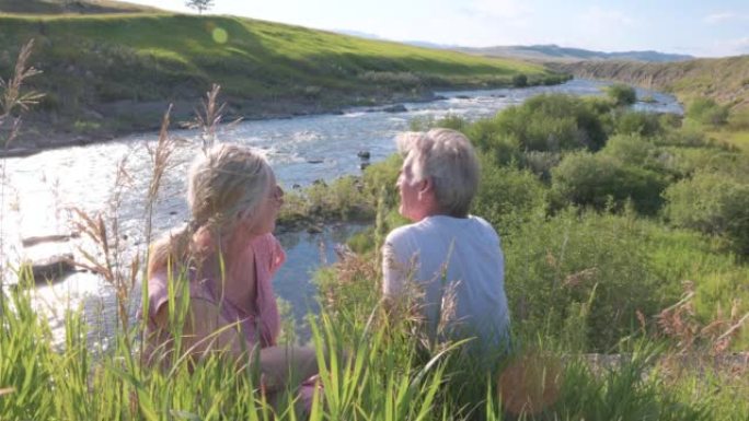 成熟的夫妇在河边的草丛中放松，远处的山脉