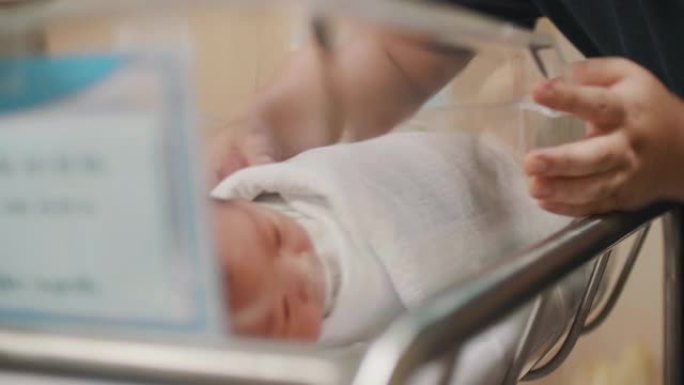 快乐的父亲在医院的托儿所里看着他的新生婴儿