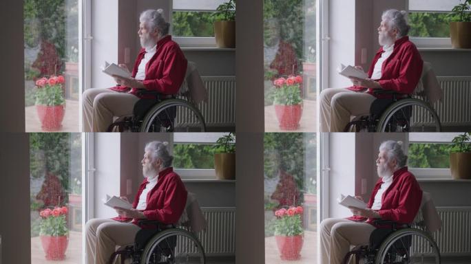坐在轮椅上的高级残疾人在雨天看着窗外。聪明的残疾高加索退休人员的肖像在家中享受文学作品。慢动作。