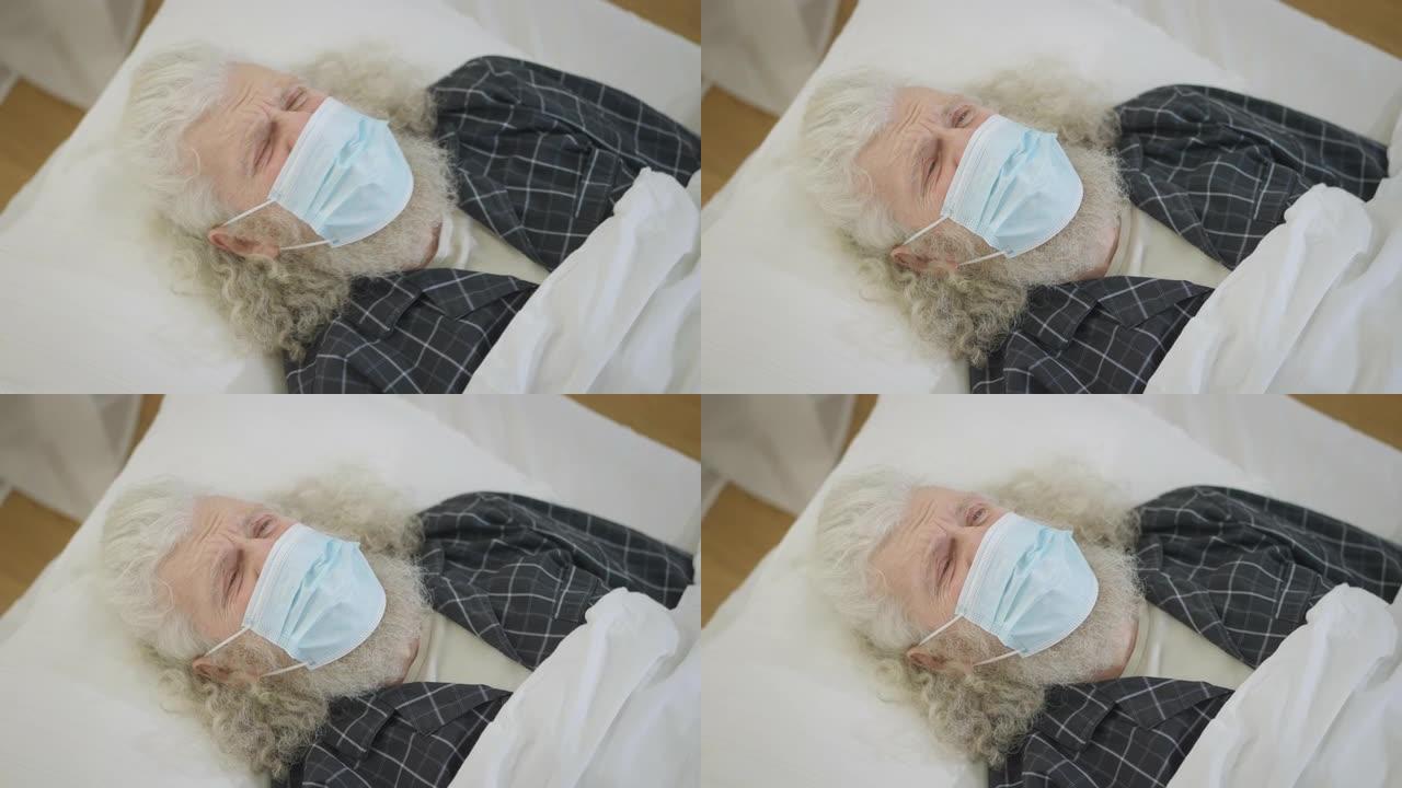 生病悲伤的白人老人躺在床上，戴着冠状病毒面罩咳嗽。疲惫疲惫的男性退休人员，在家中出现Covid-19