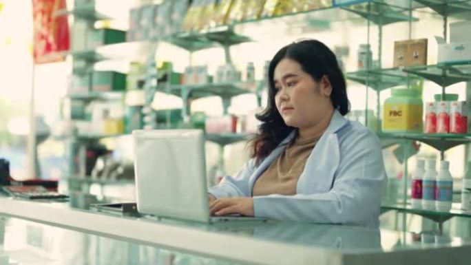 亚洲女药剂师在药房柜台使用笔记本电脑时拿着药物