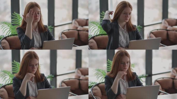 在笔记本电脑上工作的体贴的红发女人在办公室寻找解决问题的想法，认真的女人寻找灵感使决策感到缺乏想法