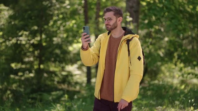 男子徒步旅行者在森林里享受周末时使用智能手机。手机上迷人的男人背包客规划森林旅行路线的低角度视图