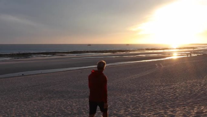 男子在日落天空下沿着空旷的海滩散步