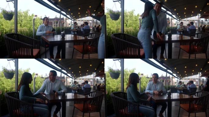 一家餐馆的年轻人在智能手机上发短信，直到他的约会对象到达时亲吻脸颊，同时举手准备点菜