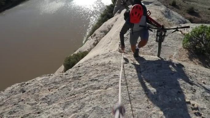 男性山地自行车手使用绳索帮助将峡谷边缘提升到河上