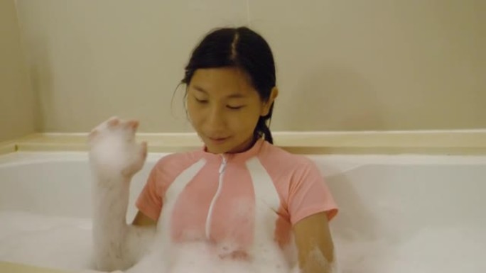 快乐的亚洲女孩在与家人度假期间享受酒店房间浴缸里的浴缸炸弹泡泡，生活方式理念。